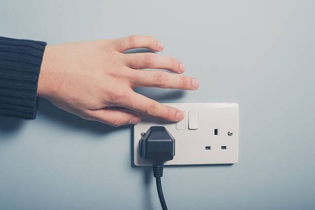 A male hand is pushing a switch on a wall socket