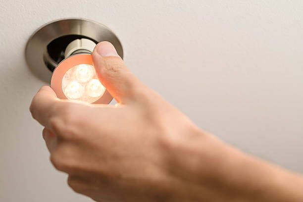 A male hand is installing an illuminated LED light bulb into a ceiling can fixture.